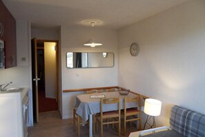 Cocina compacta con un lavamanos y una zona de comedor con mesa y sillas. Hay un espejo en la pared sobre la mesa y un reloj en la pared a la derecha.