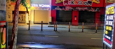 A street view at night with a brightly lit building featuring a 'My Kingdom' sign, a 'Star Wedding' sign, and a 'Hotel' sign with pricing information.