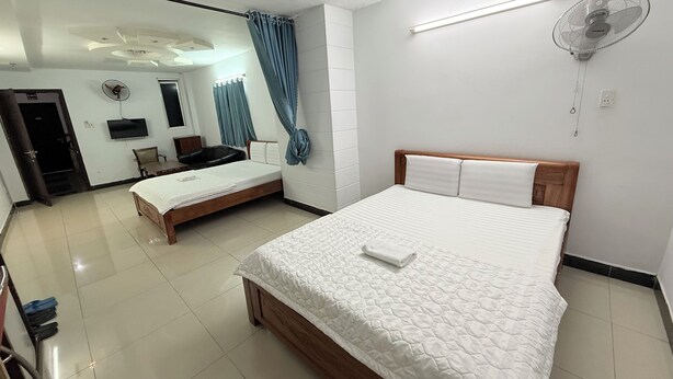 A hotel room with a large bed, a smaller bed, a desk, a chair, a TV, and a ceiling fan. - Nhu Y Hotel (Ho Chi Minh City)