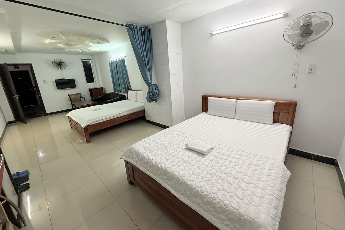 Habitación de hotel con una cama grande, una cama más pequeña, un escritorio, una silla, un televisor y un ventilador de techo.