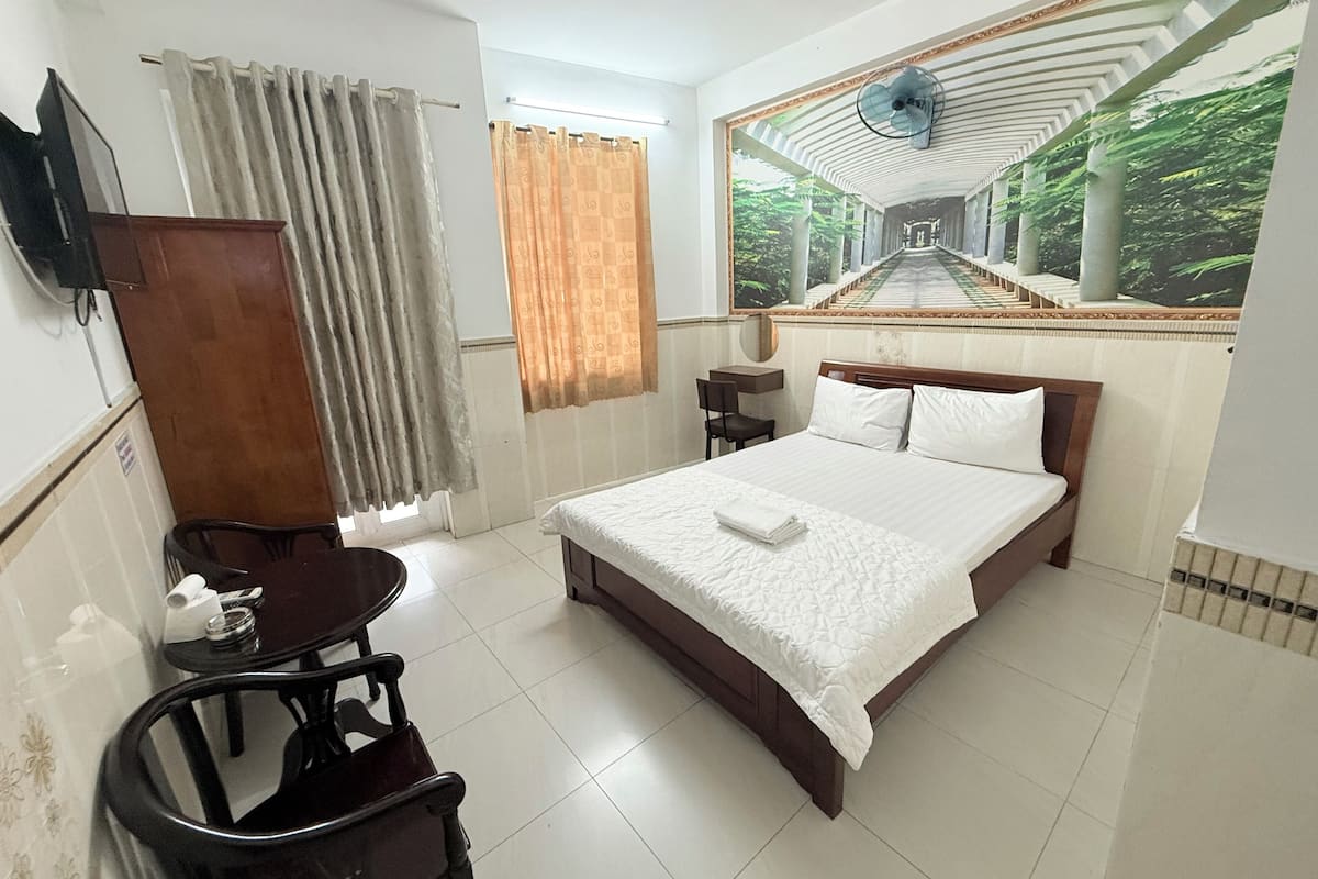 Habitación de hotel con cama, escritorio, silla, televisor y un amplio ventanal con vista a un puente.