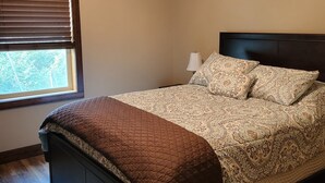 A bedroom with a bed, a ceiling fan, a window with blinds, and a nightstand with a lamp. - Heron cabin (eureka)