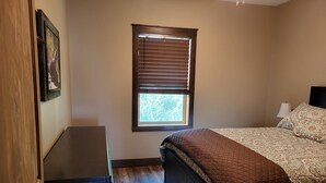 A bedroom with a bed, a window with blinds, a bedside lamp, and a dresser. - Heron cabin (eureka)