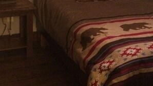Un dormitorio con cama, mesita de noche, lámpara y un cuadro en la pared.