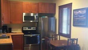 Una cocina compacta con armarios de madera, microondas, estufa, refrigerador y una mesa de comedor con sillas.