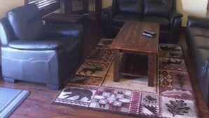 Una sala con televisor, dos sofás de cuero negro, una mesa de centro de madera y una alfombra estampada.