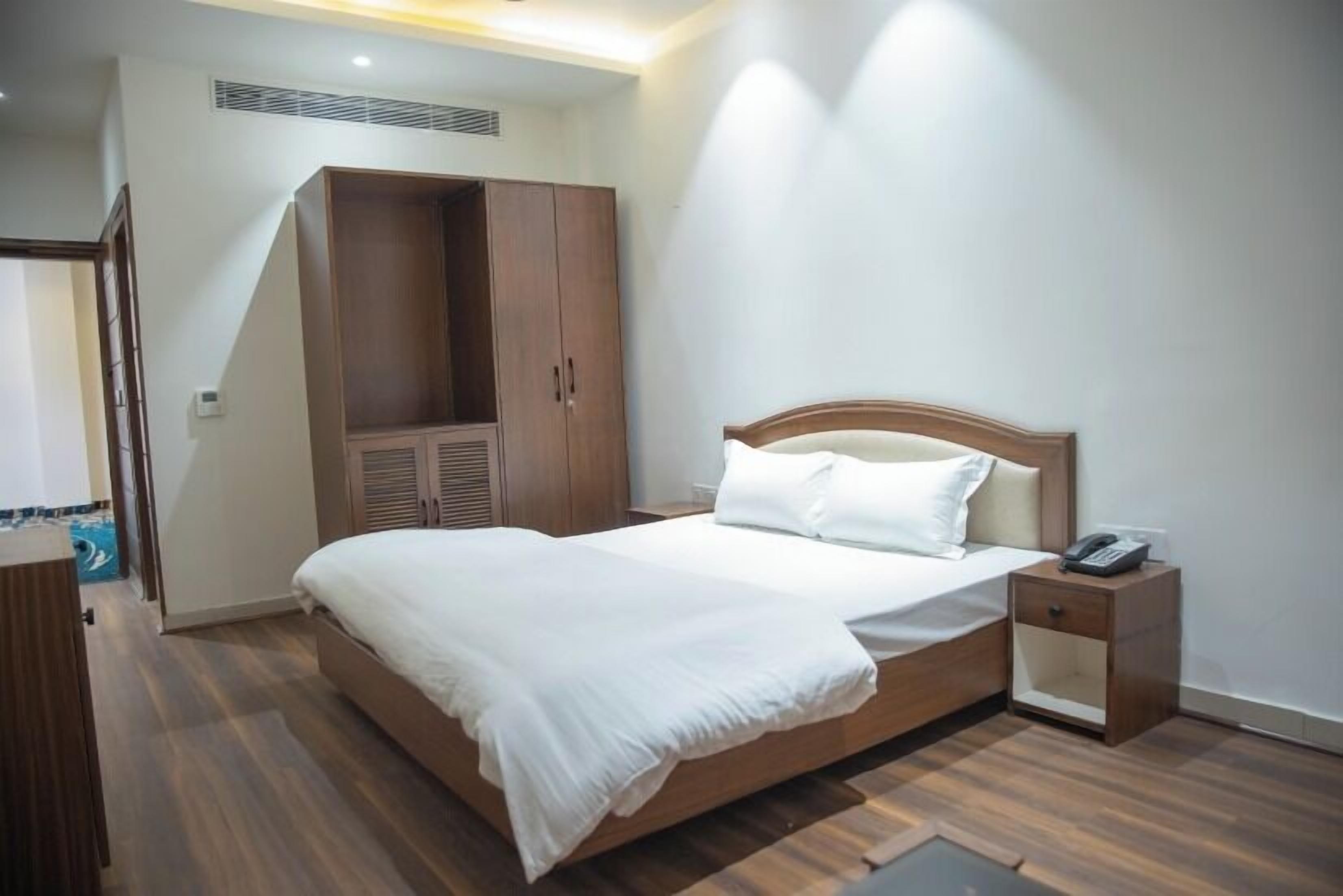 A bedroom with a bed, a wardrobe, a bedside table with a phone, and a small table.