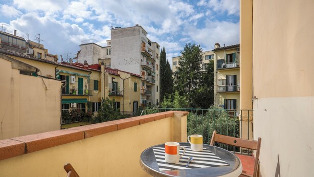A balcony with a round table and two chairs, overlooking a cityscape with buildings and trees. - Angelico Urban Loft (Florence)