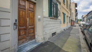 A narrow street with parked cars on one side and a building with a wooden double door and green shutters. - Angelico Urban Loft (Florence)