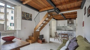A compact living space with a wooden staircase, a dining area with a table and chairs, a kitchen with white cabinets, and a green sofa. - Angelico Urban Loft (Florence)