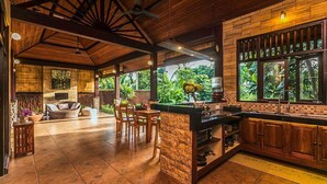 A spacious kitchen with a stone island, wooden cabinets, and large windows offering a view of greenery. - Jungle Villa - Two Bedroom Villa, Sleeps 4 (Sayan)