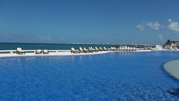 A pool area with lounge chairs and a view of the ocean.