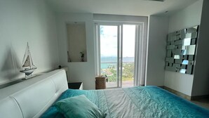 A bedroom with a large bed, a view of the sea through a sliding door, and a modern mirror wall.
