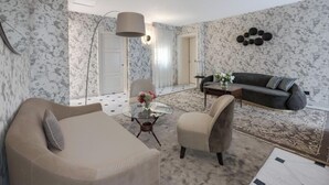 A living room with a sofa, armchair, and coffee table, a dark-colored sofa, a patterned rug, and a wall-mounted light fixture. - Exquisite 2-Bedroom Luxury Apartment in Piazza della Signoria (Firenze)