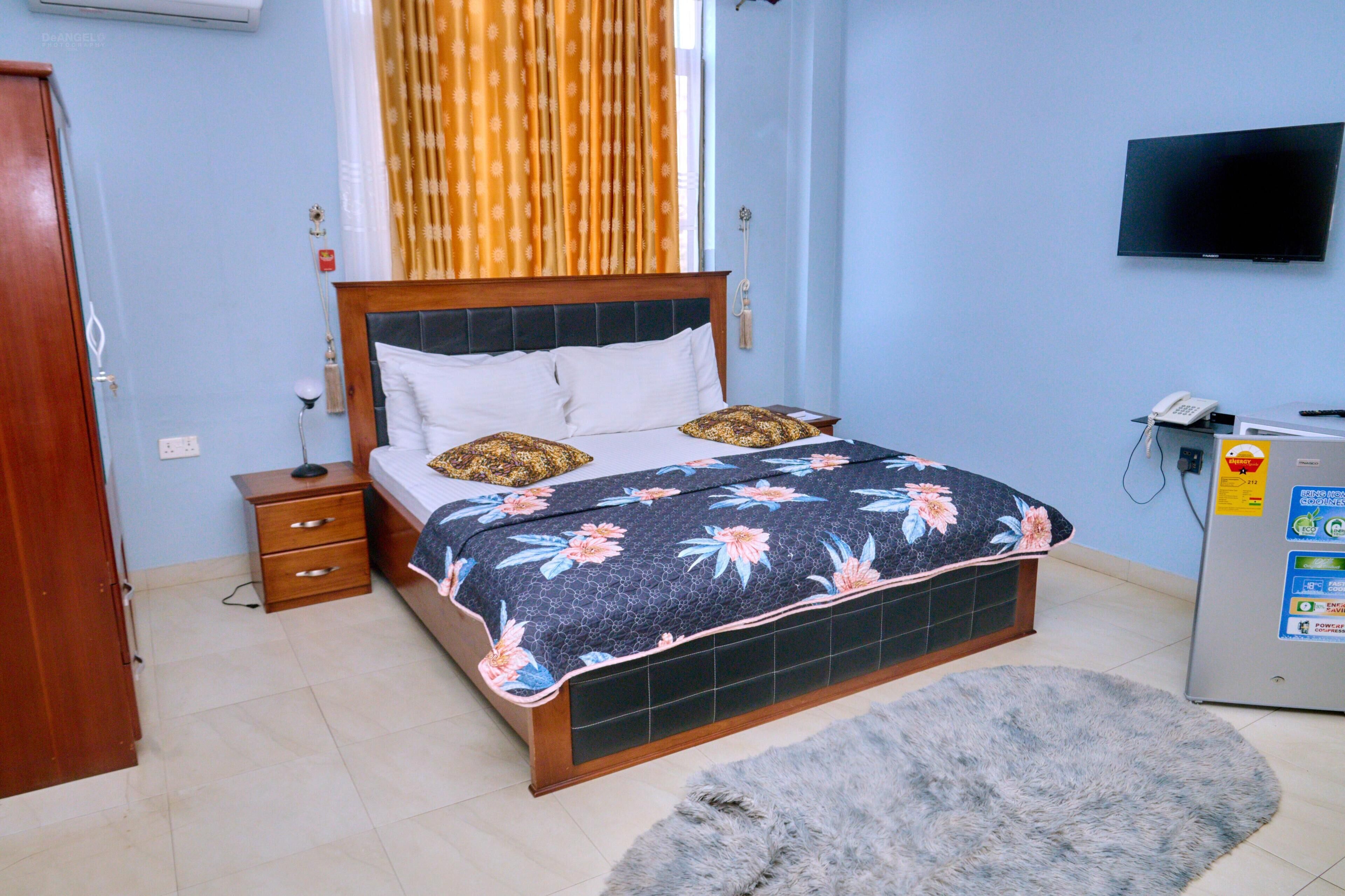 Een slaapkamer met een bed, nachtkastje en een aan de muur bevestigde televisie.