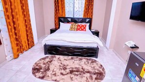 A bedroom with a bed, curtains, a TV, and a rug. - Thy Favour Hotel (Sekondi-Takoradi)