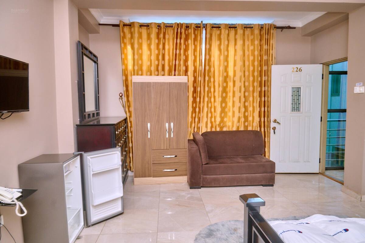 Habitació amb un sofà marró, un armari de fusta, una televisió penjada a la paret i una porta amb el número 226.