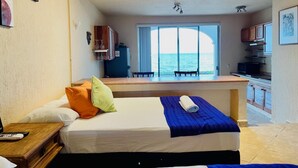 Una habitación con cama, un escritorio pequeño, una ventana con vista al mar y una kitchenette.