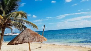Una playa con una sombrilla de paja, sillas de descanso y una vista despejada del océano.
