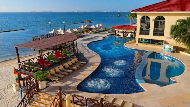 Zona de piscina en un complejo turístico, con un diseño curvo, sillas de descanso, sombrillas y vistas al mar.