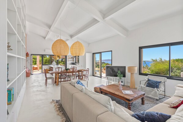 A spacious living area with a large window, a dining table, and a sofa.