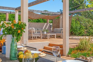 An outdoor patio with a wooden deck, seating area, and a pergola structure.