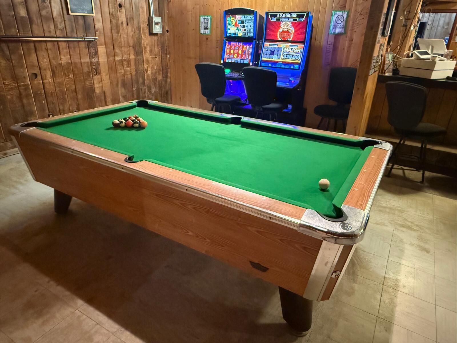 Une table de billard avec des billes, un mur en bois et des machines à sous en arrière-plan.