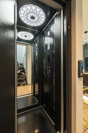An elevator with a starry ceiling design, a control panel, and a reflection of marble stairs.