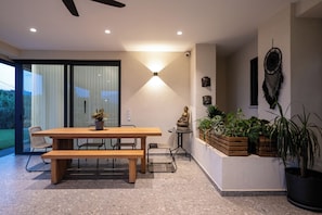 Un interior moderno con una mesa de comedor de madera, sillas, un banco, una estatua de Buda y plantas en macetas.