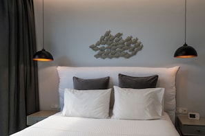 A neatly made bed with white linens, two pillows, a wall-mounted light fixture, and a power outlet on the nightstand.