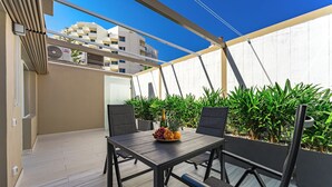 Un patio al aire libre con una mesa dispuesta para dos personas, rodeada de sillas y una vista de un paisaje urbano al fondo.