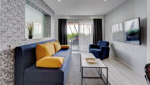 Una sala de estar moderna con un sofá azul, cojines amarillos, una mesa de centro y un televisor en la pared.