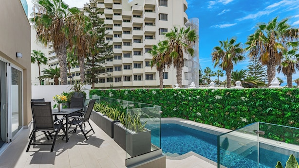 Zona de piscina en la azotea con barandilla de vidrio, mobiliario exterior y vista a un edificio de gran altura.