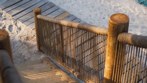 A wooden deck with a woven fence, leading to a sandy area. - Cabanas Blue (Mata de São João)
