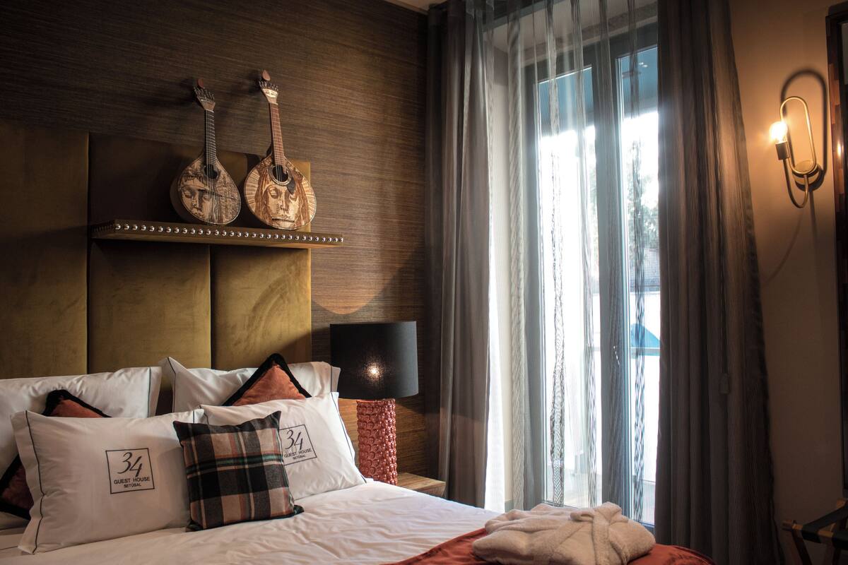 Habitación de hotel con cama, almohadas, cabecero, lámpara y ventana con cortinas.