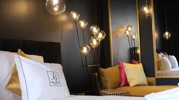 Habitación de hotel con cama, sofá, espejo y lámpara de pie con luces esféricas.