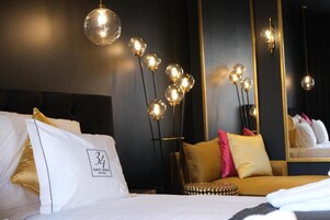 Habitación de hotel con cama, sofá, espejo y lámpara de pie con luces esféricas.