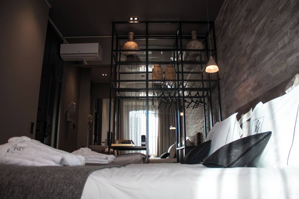 Habitación de hotel con una cama grande, un escritorio y un espejo. Se observa un equipo de aire acondicionado en la pared y un colgador de luz.