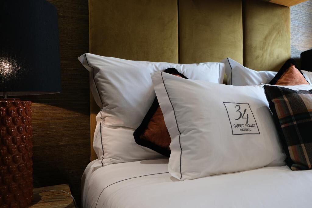 A hotel room with a bed, pillows, and a lamp.