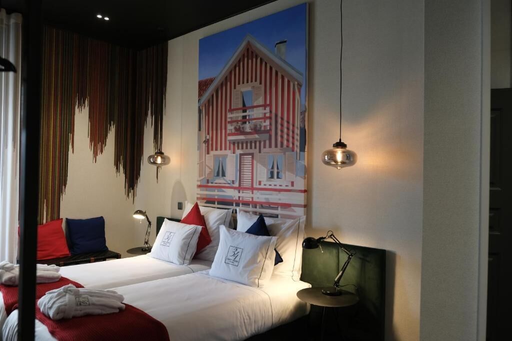 Una habitación de hotel con dos camas, un cuadro grande de un granero y una lámpara colgante.