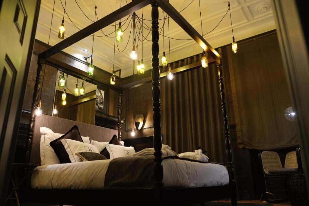 Ein Bett mit Baldachin, mehrere hängende Lampen und ein Sessel in einem gemütlich beleuchteten Raum mit Holzwänden und einem großen Spiegel.