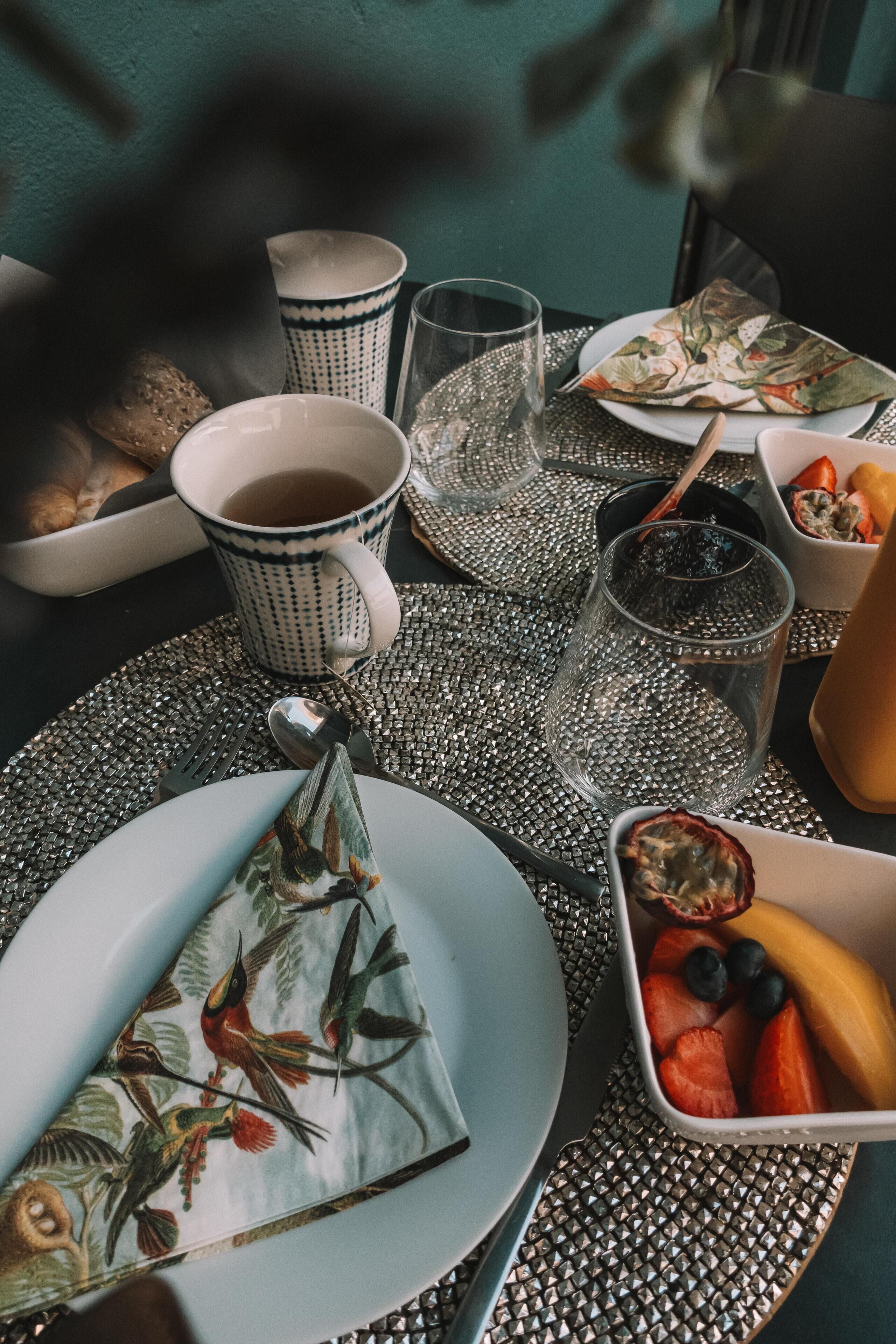 A table set with a plate, a cup, a glass, and a bowl of fruit.