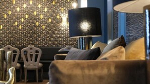 En moderne stue med en mørkeblå væg, tapet med mønster, en gulvlampe i sort og en sofa med puder.
