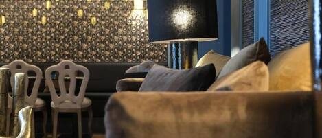 Una sala de estar moderna con una pared azul oscuro, un papel tapiz estampado, una lámpara de pie negra y un sofá con cojines.