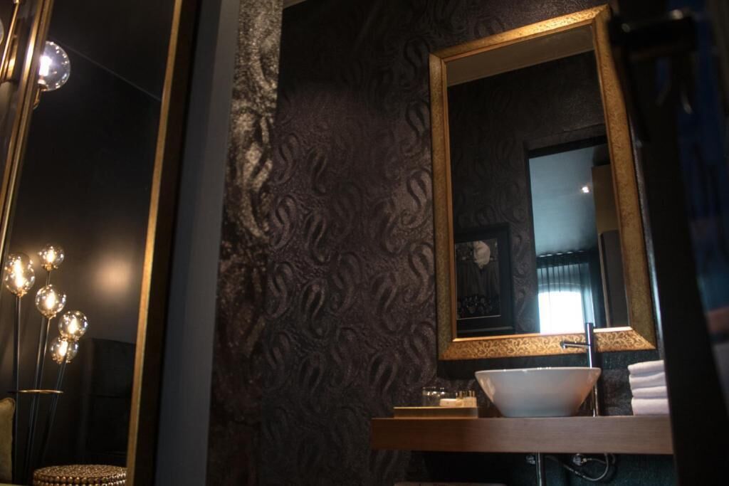 A bathroom with a large mirror, a sink, and a decorative light fixture.