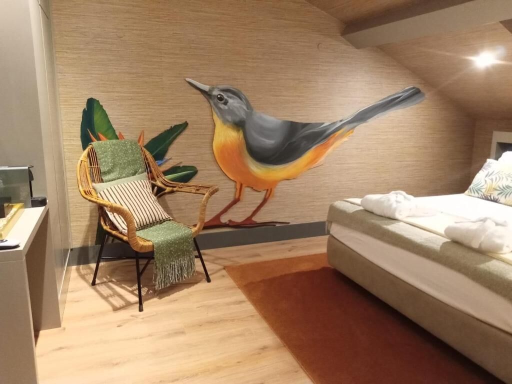 A bedroom with a bed, a chair, and a wall mural of a bird.