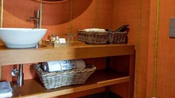 A bathroom with a round mirror, a white sink, a wooden vanity, a wicker basket, and a toilet.