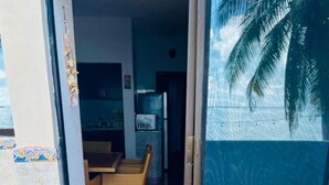 A room with a tiled floor, a wicker chair, and a glass door leading to an outdoor area with a palm tree. - Punta me beautifull Apartment beach front (Cancun)