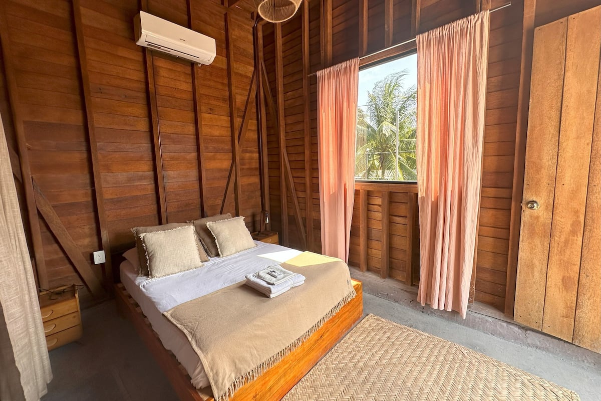 A wooden room with a bed, a window with curtains, and an air conditioning unit.