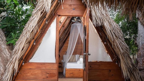 Une structure triangulaire en bois, dotée d’un lit et d’une moustiquaire.
